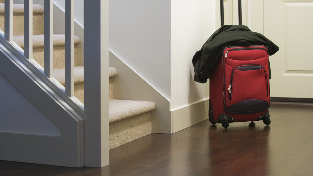 A red suitcase with a coat by the front door of a house