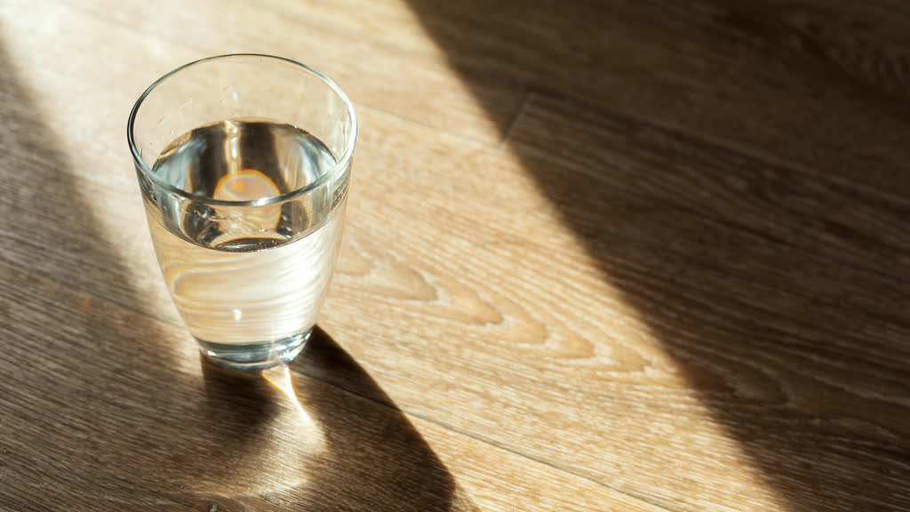 A glass of water on a wooden table in morning light