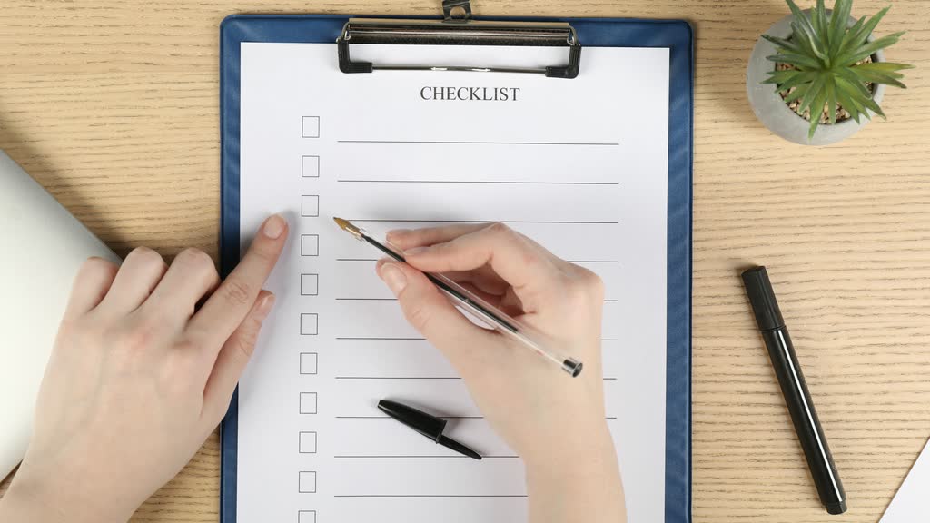 A hand ticking items on a printed checklist on a clipboard