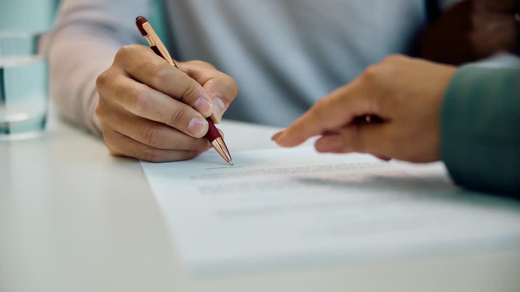 Hands signing a document on a white table