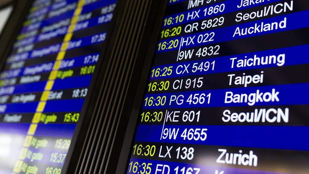 An airport departures board listing flights to Bangkok and other cities