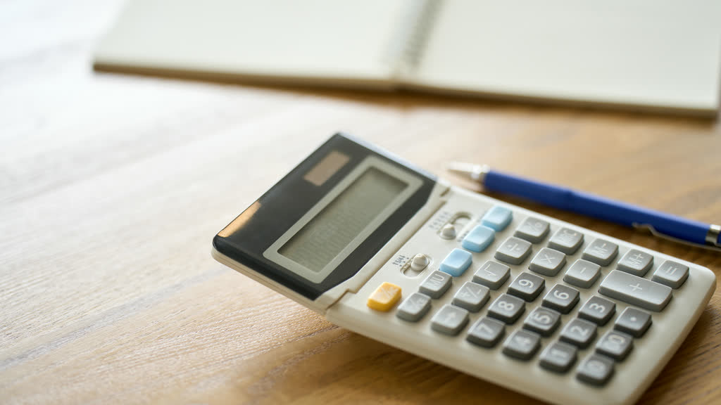 A calculator, a pen and a notebook on a wooden table