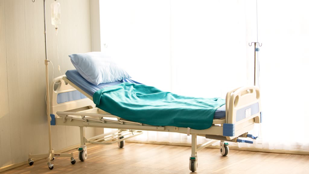 An empty hospital bed with an IV stand in a bright room