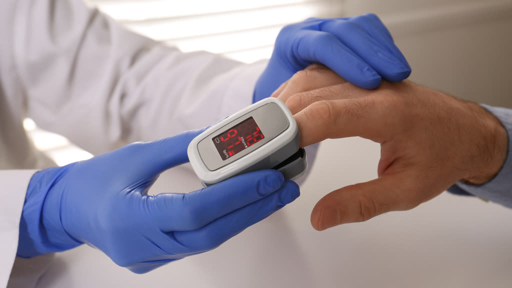 A clinician in blue gloves clipping a pulse oximeter onto a patient's finger