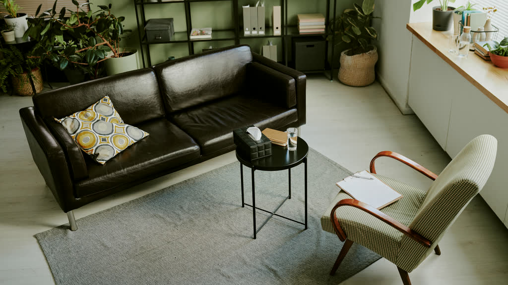 A quiet therapy room with a leather sofa, an armchair and plants