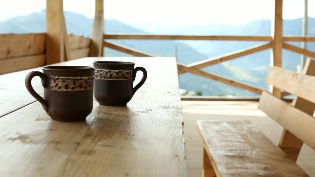 Two ceramic mugs on a wooden table with mountains in the background