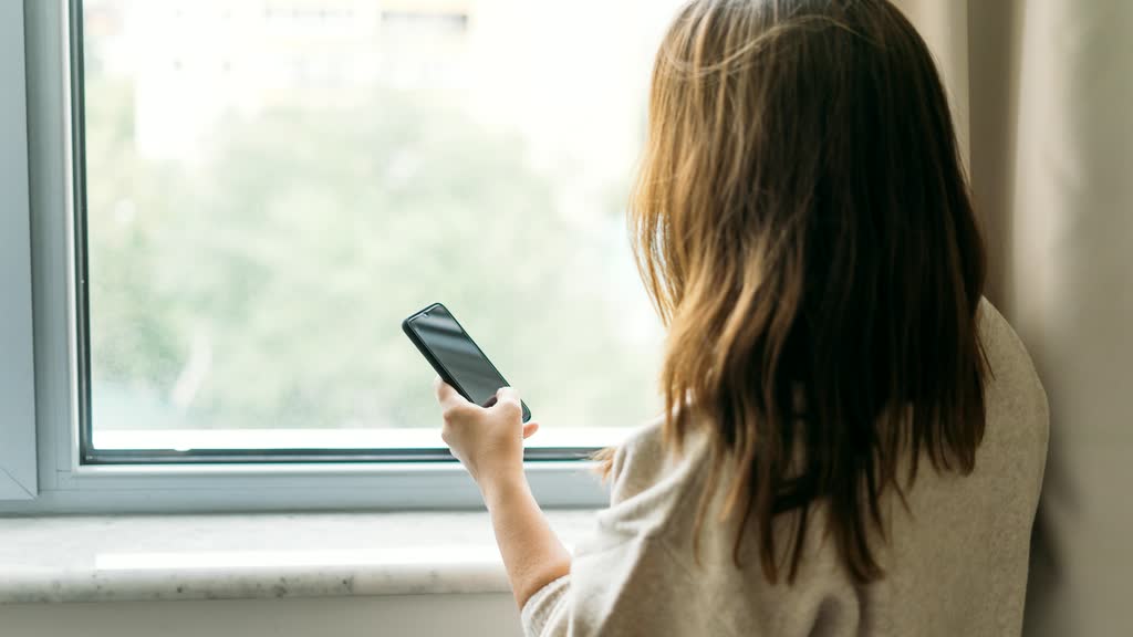 A woman on her phone by a window, seen from behind