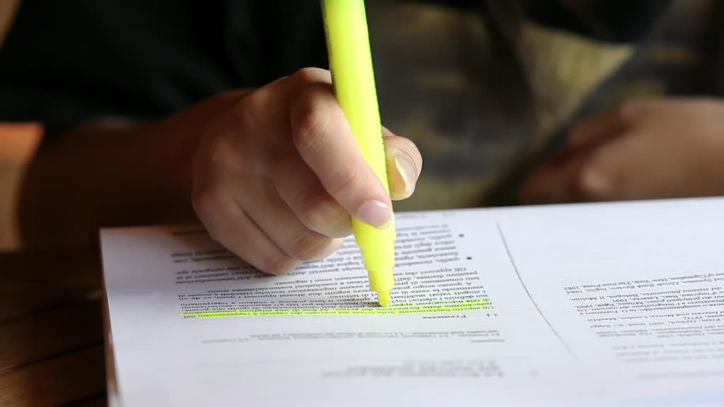 A hand marking a line of printed text with a yellow highlighter
