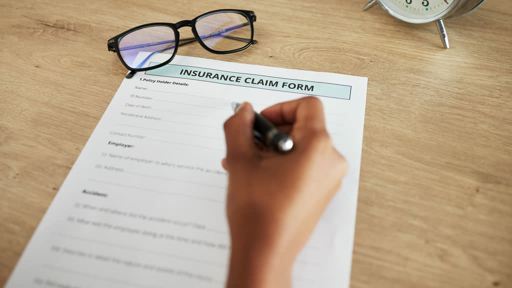 A hand filling in a printed insurance claim form