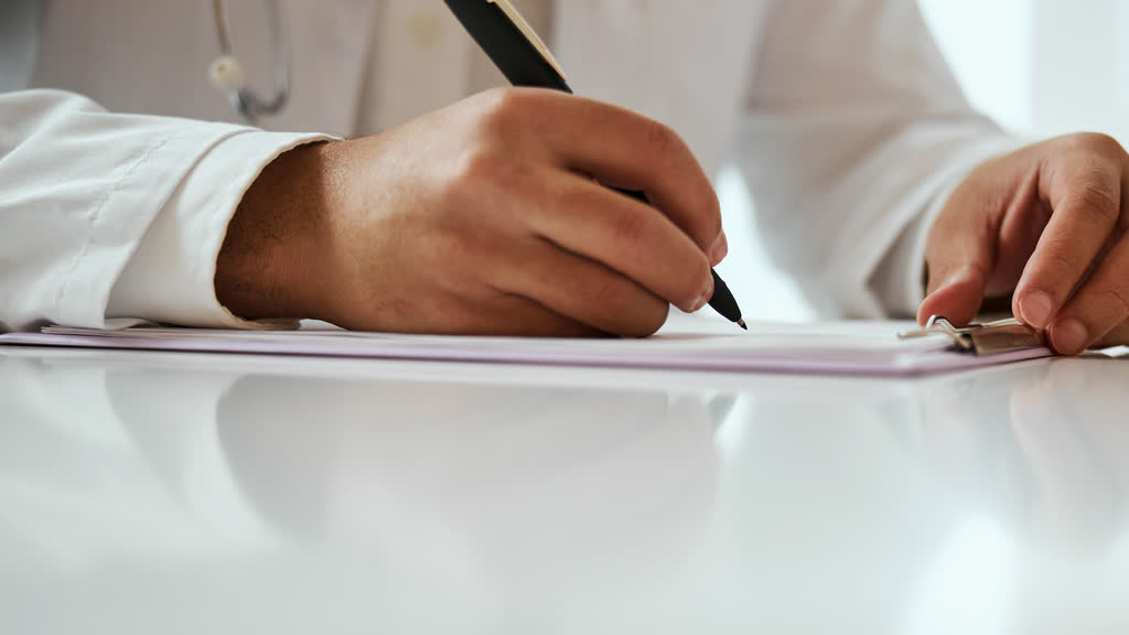 A doctor's hands writing on a clipboard at a white desk