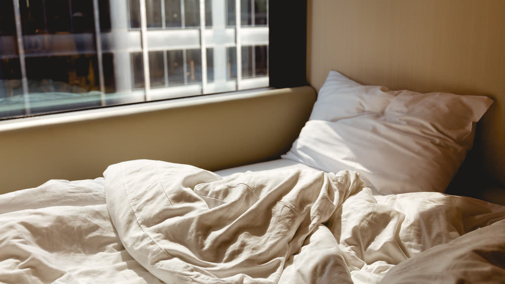 An unmade bed in morning sunlight from a window