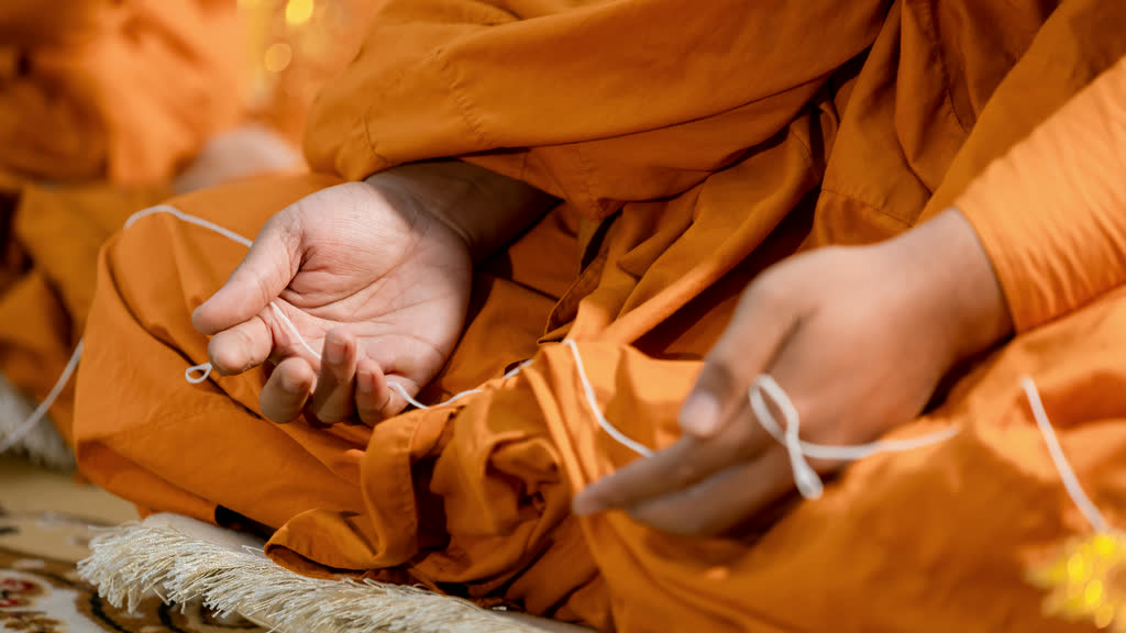 A Buddhist monk's hands holding a white sacred thread during a ceremony in Thailand