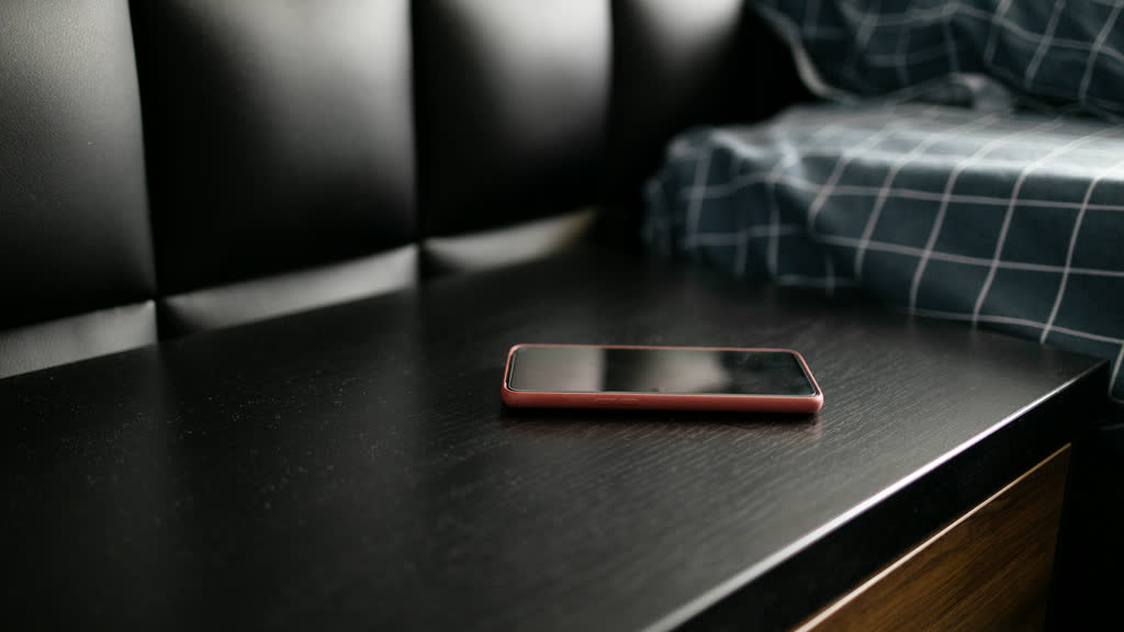 A smartphone with its screen off on a dark bedside table