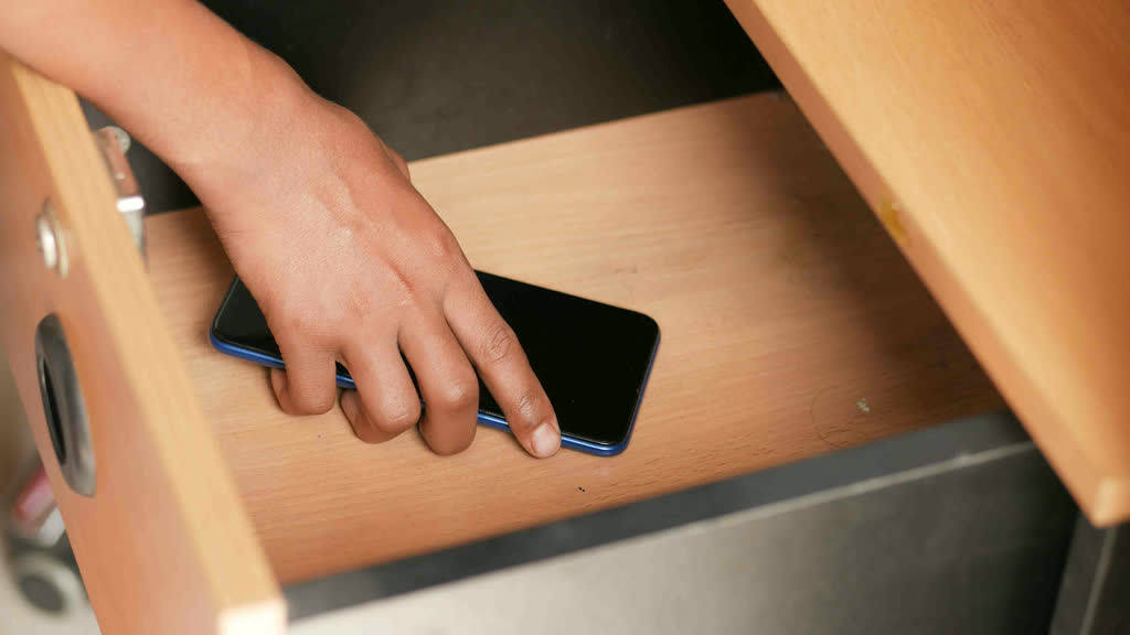 A hand putting a smartphone away in a wooden drawer