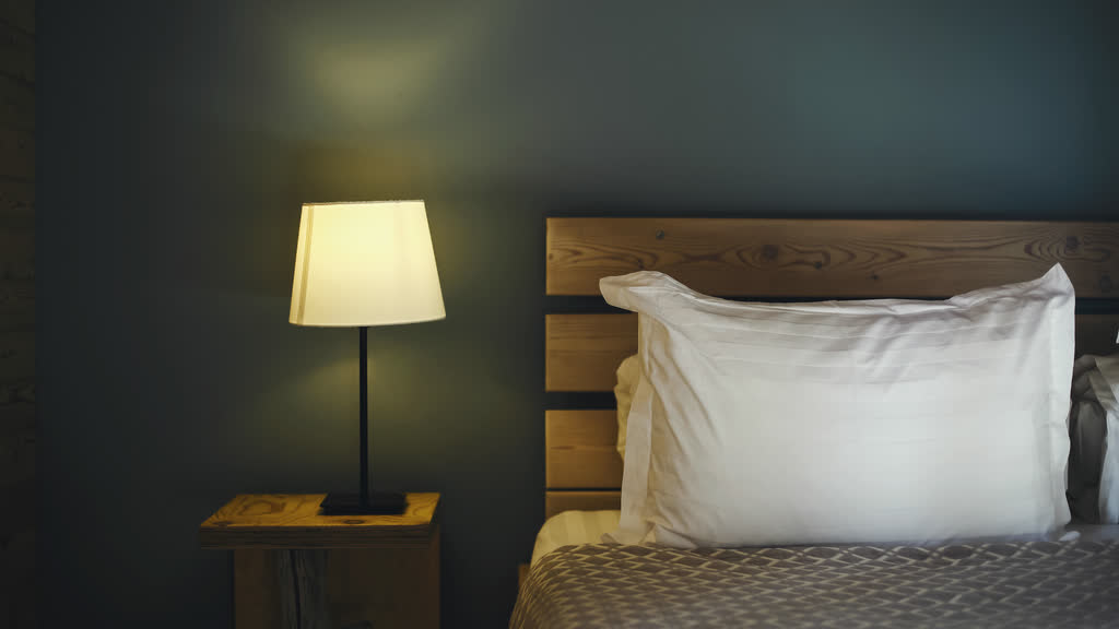 A quiet bedroom lit by a bedside lamp