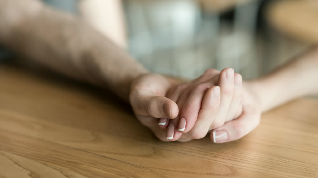 Two people holding hands on a wooden table